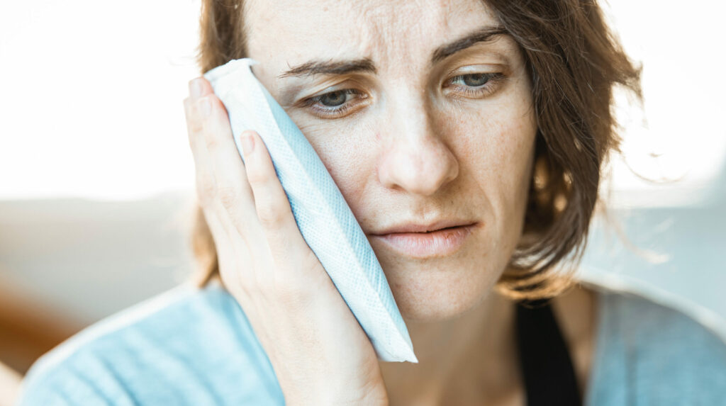 Woman using ice pack on her cheek to help with oral surgery swelling and pain